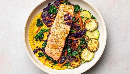 Salmon over greens and zucchini in a bowl