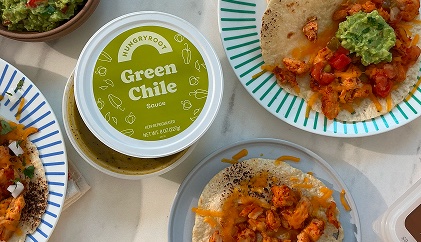 Green chile salsa with tacos and dips spread on a table