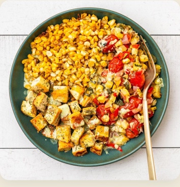 A corn, tomato, and tofu bowl with a gold spoon