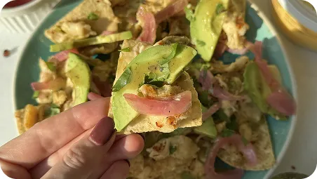 Hand holding a piece of food with avocado and red onion
