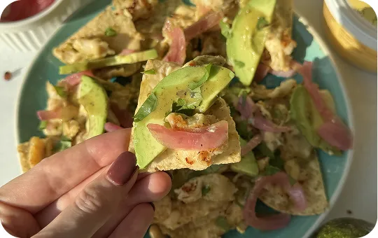 Hand holding a piece of food with avocado and red onion